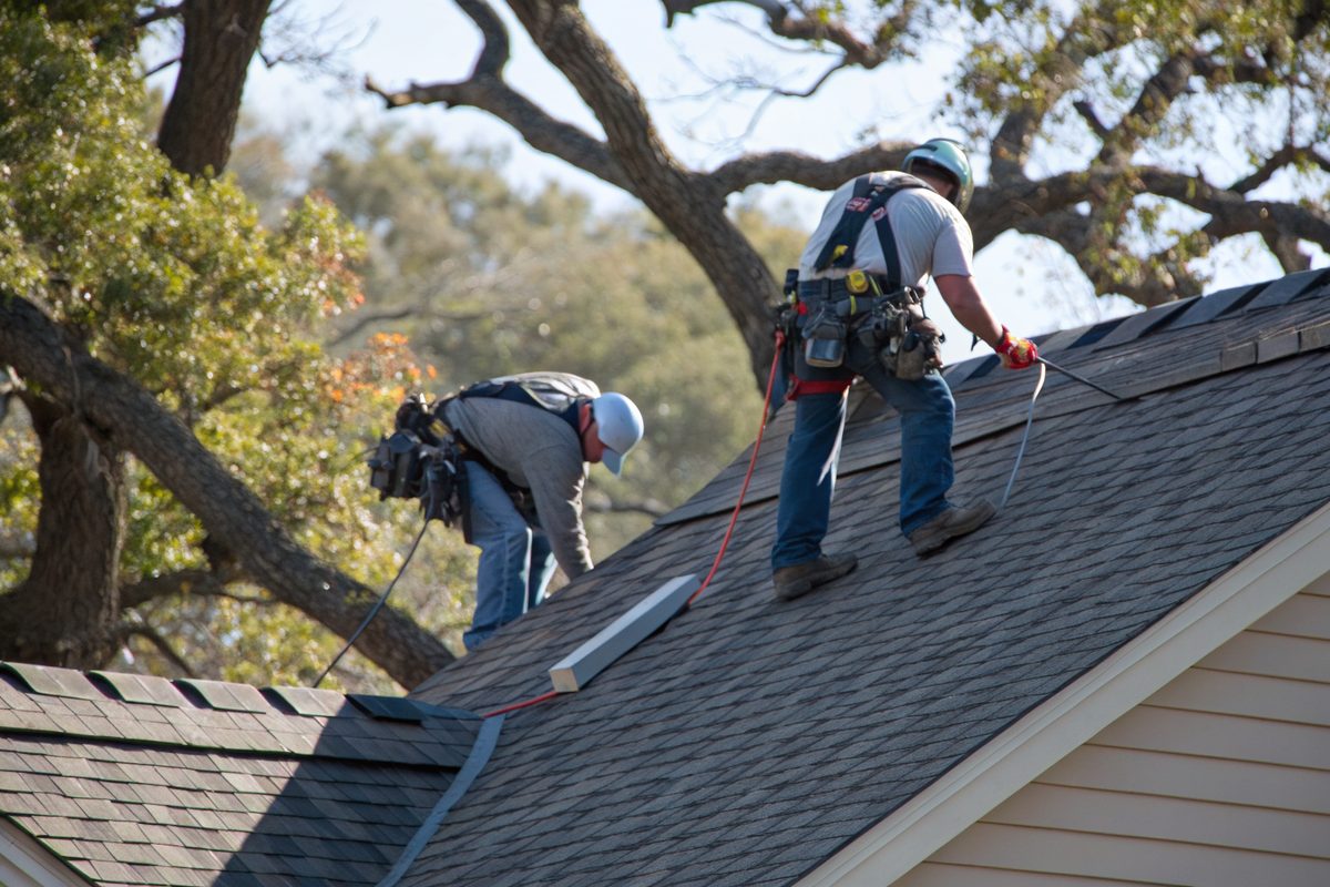 Two roofers laying new shingles on a ranch roof